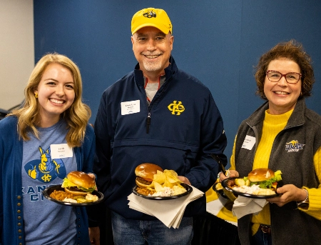 Pharmacy alumni dressed in their UMKC gear smile at the camera while attending a school sponsored tailgate event.