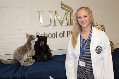 Student at Pharmacy Camp poses in white coat at a table with stuffed kangaroos
