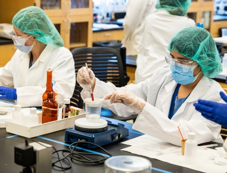 Two students dressed in lab attire while working in a pharmacy lab during UMKC's Pharmacy Camp.