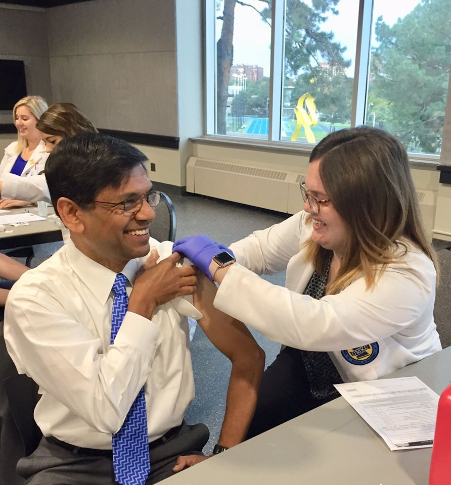 UMKC Chancellor gets a flu shot from a pharmacy student in a white jacket