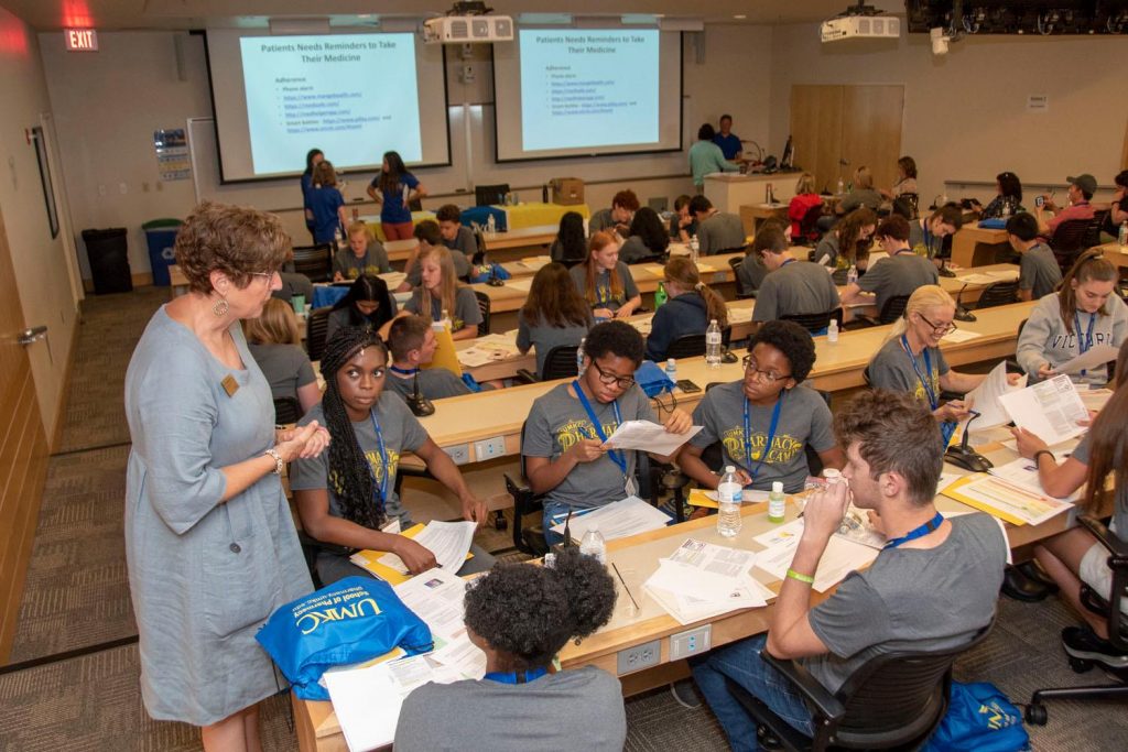 An instructor stands next to a table of students working on an activity at the 2019 Pharmacy Camp